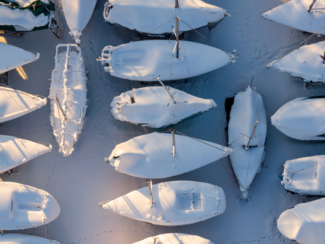 Aerial view of sailboats covered in thick white snow at a winter boatyard with long shadows during sunset in Trakai Vilnius County Lithuania. Aerial view of sailboats covered in thick white snow at a winter boatyard with long shadows during sunset in Trakai Vilnius County Lithuania.