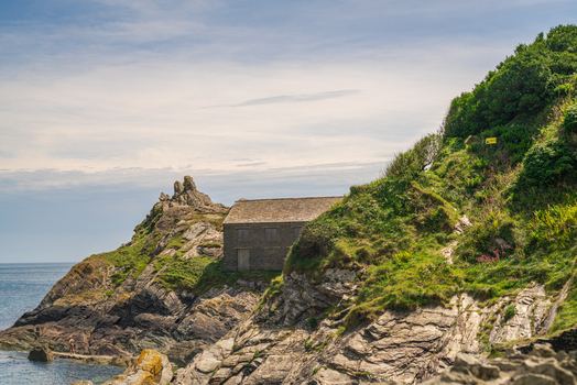 View of a historic stone building perched on the rugged cliffs overlooking the sea in the coastal village of Polperro Cornwall United Kingdom. View of a historic stone building perched on the rugged cliffs overlooking the sea in the coastal village of Polperro Cornwall United Kingdom.