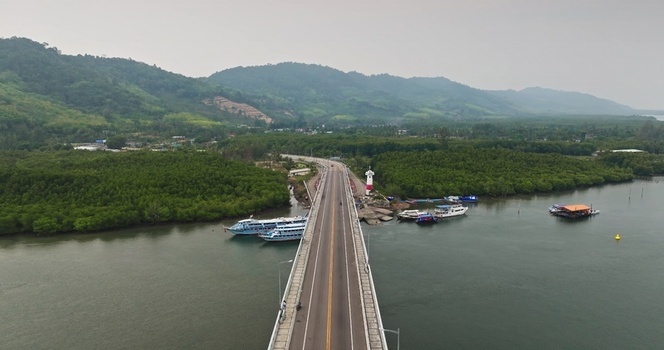 Aerial view of a bridge spanning a river with docked boats and lush green hills in the background in Thailand. Aerial view of a bridge spanning a river with docked boats and lush green hills in the background in Thailand.