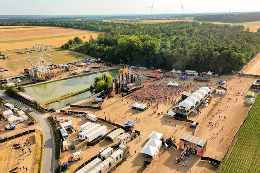 Herzogenaurach Germany 22 July 2022 Aerial view of the Open Beatz Festival featuring a large stage a Ferris wheel and crowds of people surrounded by forests and wind turbines. Herzogenaurach Germany 22 July 2022 Aerial view of the Open Beatz Festival featuring a large stage a Ferris wheel and crowds of people surrounded by forests and wind turbines.