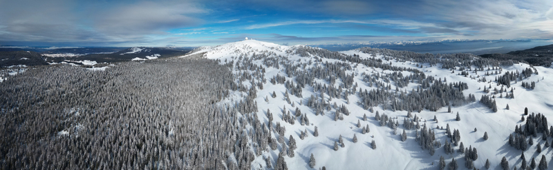 Aerial view of snow blanketed trees cascade down the mountain slopes towards the town below a stark white contrast against the dark forest Mijoux Auvergne Rhône Alpes France. Aerial view of snow blanketed trees cascade down the mountain slopes towards the town below a stark white contrast against the dark forest Mijoux Auvergne Rhône Alpes France.