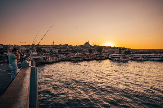 Istanbul Turkiye 02 October 2019 View of the Galata Bridge bustling with activity as the setting sun casts a golden glow over the Yeni Cami mosque.