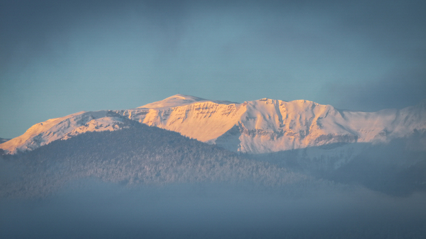 Aerial view of snow capped mountain peaks glowing in golden sunlight above a thick layer of mist in Vesancy Auvergne Rhone Alpes France. Aerial view of snow capped mountain peaks glowing in golden sunlight above a thick layer of mist in Vesancy Auvergne Rhone Alpes France.