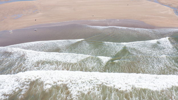 Aerial view of Bantham Beach with white waves crashing on the sandy shore and surfers walking on the sand in Kingsbridge Devon United Kingdom. Aerial view of Bantham Beach with white waves crashing on the sandy shore and surfers walking on the sand in Kingsbridge Devon United Kingdom.
