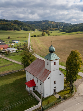 Aerial view of a charming white church with a vivid red roof and green dome nestled amidst golden autumn fields and rolling hills under a dramatic sky Haj Zilina Region Slovakia. Aerial view of a charming white church with a vivid red roof and green dome nestled amidst golden autumn fields and rolling hills under a dramatic sky Haj Zilina Region Slovakia.