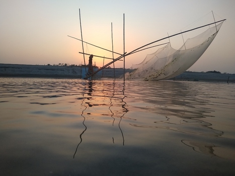 View of a traditional fishing net with a fisherman standing on a wooden platform during sunset on the river in Kushtia Khulna Division Bangladesh. View of a traditional fishing net with a fisherman standing on a wooden platform during sunset on the river in Kushtia Khulna Division Bangladesh.