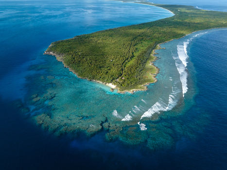 Aerial view of a lush green island surrounded by turquoise waters and white waves crashing against the shore Ouvéa Loyalty Islands Province New Caledonia. Aerial view of a lush green island surrounded by turquoise waters and white waves crashing against the shore Ouvéa Loyalty Islands Province New Caledonia.