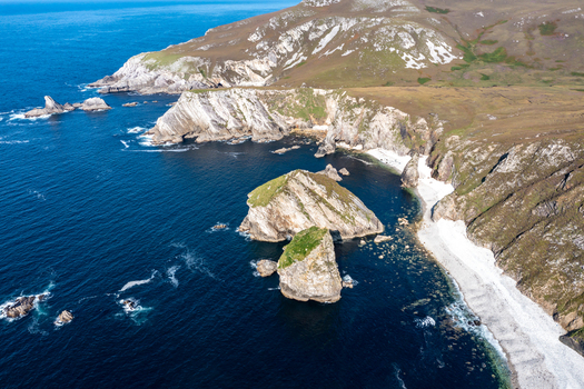 Aerial view of the dramatic sea stacks and rugged cliffs of Glenlough Bay featuring deep blue Atlantic waters along the coastline in Ardara County Donegal Ireland.