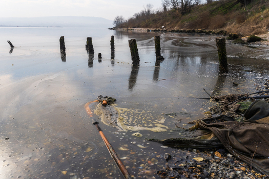 View of Lake Varna shoreline with weathered wooden posts protruding from the water scattered debris and pebbles along the bank Varna Bulgaria. View of Lake Varna shoreline with weathered wooden posts protruding from the water scattered debris and pebbles along the bank Varna Bulgaria.