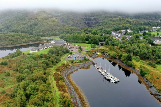 Aerial view of Glencoe featuring a marina with sailboats in a calm inlet surrounded by lush green hills forests and buildings Glencoe Scotland United Kingdom.