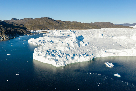 Aerial view of Ilulissat glacier with massive icebergs floating in deep blue water near the rocky coastline of Greenland. Aerial view of Ilulissat glacier with massive icebergs floating in deep blue water near the rocky coastline of Greenland.