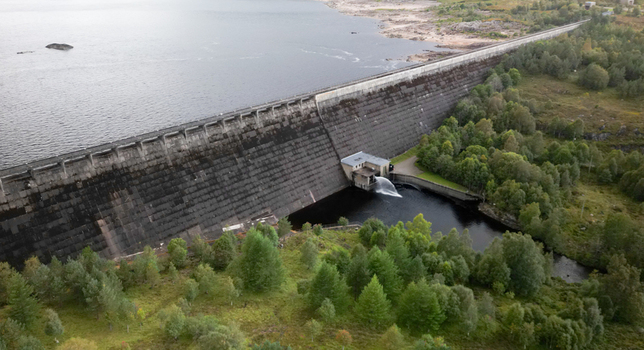 Aerial view of Cluanie Dam with water discharging from the reservoir surrounded by lush green forests and rolling hills in Inverness Scotland United Kingdom.