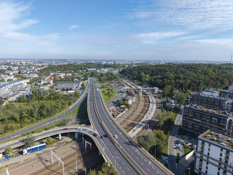 Aerial view of a highway interchange and railway tracks running through urban surroundings with modern buildings and green trees under a blue sky in Krakow Lesser Poland Voivode Poland.