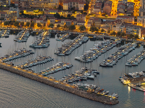Aerial view of the marina filled with sailboats and yachts moored along the stone breakwater with illuminated city buildings in Antibes Provence Alpes Cote d Azur France. Aerial view of the marina filled with sailboats and yachts moored along the stone breakwater with illuminated city buildings in Antibes Provence Alpes Cote d Azur France.