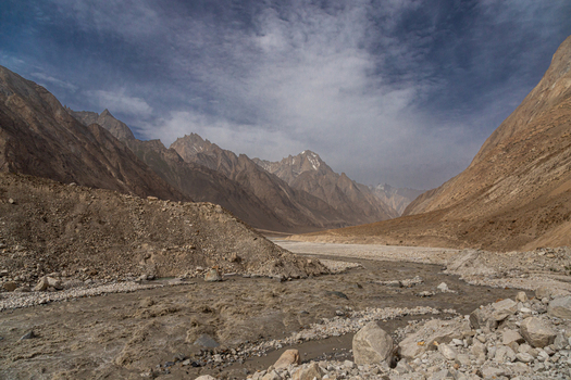 View of the rugged landscape surrounding the Baltoro Glacier featuring a glacial river flowing through rocky terrain under a cloudy sky in Baltoro Gilgit Baltistan Pakistan.