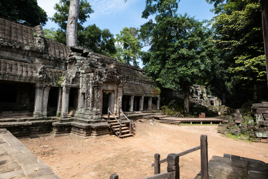 View of the ancient stone ruins of Ta Prohm temple with massive tree roots growing over the walls surrounded by lush jungle foliage in Krong Siem Reap Siem Reap Province Cambodia. View of the ancient stone ruins of Ta Prohm temple with massive tree roots growing over the walls surrounded by lush jungle foliage in Krong Siem Reap Siem Reap Province Cambodia.