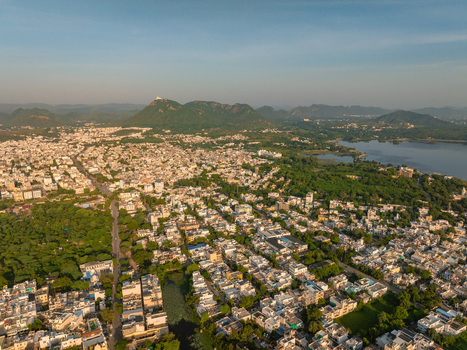 Aerial view of the historic city of Udaipur featuring dense urban architecture lush green trees and the expansive Fateh Sagar Lake in Udaipur Rajasthan India.