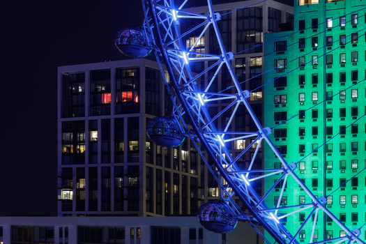 Aerial view of the London Eye at night featuring its illuminated blue structure and passenger capsules against the backdrop of modern city buildings in London Greater London United Kingdom.