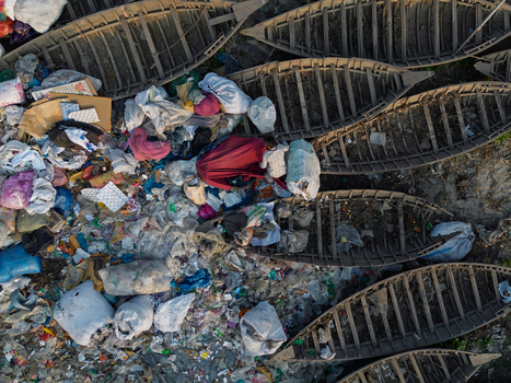 Dhaka Division Bangladesh 23 January 2026 Aerial view of traditional wooden boats on the Buriganga River bank surrounded by plastic waste with a person among the debris.
