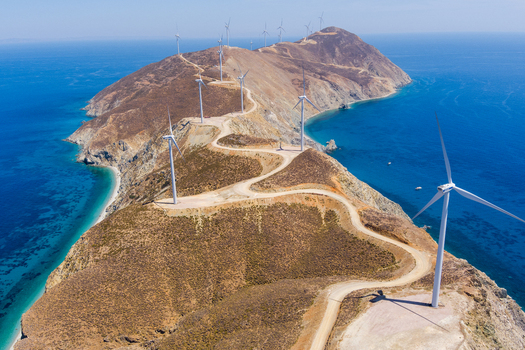 Greece 21 September 2026 Aerial view of a wind farm on a rugged coastal ridge featuring multiple wind turbines along a winding dirt road surrounded by the Aegean Sea. Greece 21 September 2026 Aerial view of a wind farm on a rugged coastal ridge featuring multiple wind turbines along a winding dirt road surrounded by the Aegean Sea.