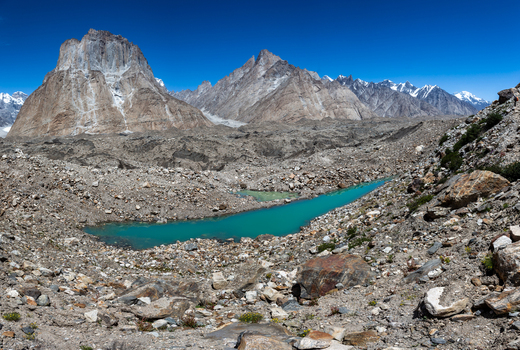 View of the turquoise glacial lake at Baltoro Glacier surrounded by rugged rocky terrain and towering snow capped mountain peaks in Baltoro Gilgit Baltistan Pakistan.