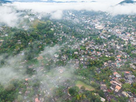 Aerial view of the dense urban landscape nestled among lush green hills and shrouded in morning mist and low clouds over Kandy Central Province Sri Lanka. Aerial view of the dense urban landscape nestled among lush green hills and shrouded in morning mist and low clouds over Kandy Central Province Sri Lanka.