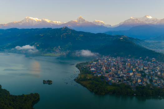 Aerial view of Phewa Lake and the city of Pokhara nestled beneath the snow capped peaks of the Annapurna mountain range in Nepal.