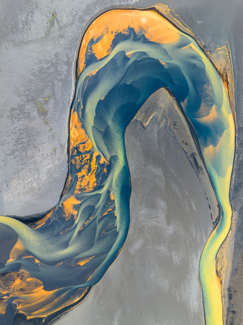 Aerial view of a braided river with vibrant blue and golden sediment patterns winding through the volcanic landscape of Iceland. Aerial view of a braided river with vibrant blue and golden sediment patterns winding through the volcanic landscape of Iceland.