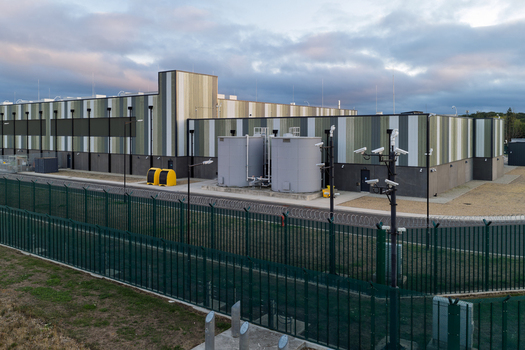 Aerial view of a modern data center facility with security fencing surveillance cameras and large storage tanks in the United Kingdom. Aerial view of a modern data center facility with security fencing surveillance cameras and large storage tanks in the United Kingdom.