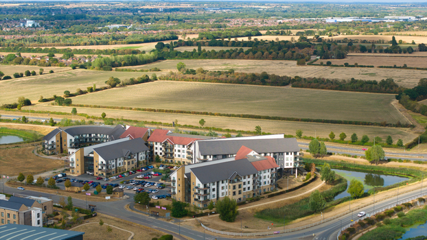 Aerial view of Wixams Retirement Village featuring modern residential buildings with pitched roofs and parking surrounded by fields roads and a pond in Bedford England United Kingdom.