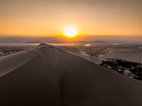 Aerial view of Huacachina oasis surrounded by vast sand dunes at sunset with golden light casting shadows over the desert landscape in Huacachina Ica Peru. Aerial view of Huacachina oasis surrounded by vast sand dunes at sunset with golden light casting shadows over the desert landscape in Huacachina Ica Peru.