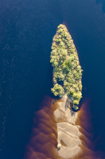 Aerial view of the Klaralven river featuring a small lush island with dense vegetation and a sandy riverbank in Varmlands lan Sweden. Aerial view of the Klaralven river featuring a small lush island with dense vegetation and a sandy riverbank in Varmlands lan Sweden.