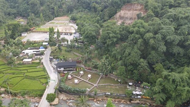 Aerial view of Kopi Tubing Cafe and Resto nestled among lush green rice paddies and dense forest along a river in Kecamatan Pamijahan Jawa Barat Indonesia. Aerial view of Kopi Tubing Cafe and Resto nestled among lush green rice paddies and dense forest along a river in Kecamatan Pamijahan Jawa Barat Indonesia.