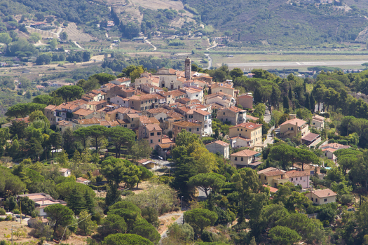 View of terracotta rooftops nestled among verdant trees a quaint village perched atop a hill bathed in warm sunlight Sant Ilario in Campo Tuscany Italy. View of terracotta rooftops nestled among verdant trees a quaint village perched atop a hill bathed in warm sunlight Sant Ilario in Campo Tuscany Italy.