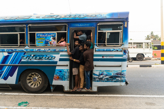Sri Lanka 15 January 2026 View of a crowded blue bus with passengers hanging out of the open doorway on a road.