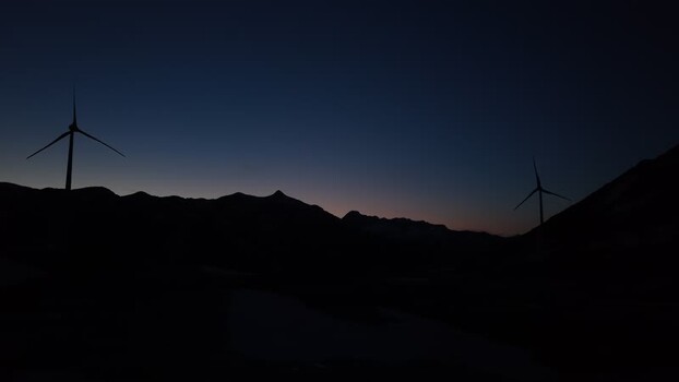 Aerial view of the silhouette of wind turbines at San Gottardo wind Park against a twilight sky over mountain ridges in Airolo Ticino Switzerland.