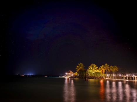 View of Likuliku Lagoon Resort at night with illuminated palm trees a wooden pier extending over the calm lagoon and a clear starry sky in Yaro Nadroga Navosa Fiji.