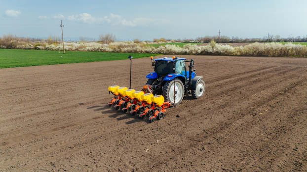 Aerial view of a blue tractor with yellow and orange components working on a field of brown soil Sremska Mitrovica Vojvodina Serbia. Aerial view of a blue tractor with yellow and orange components working on a field of brown soil Sremska Mitrovica Vojvodina Serbia.