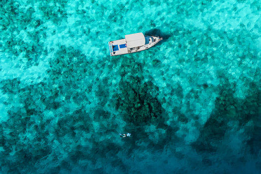 Aerial view of a boat and a snorkeler swimming in the clear turquoise water of the Indian Ocean in Vashafaru Haa Alif Atoll Maldives. Aerial view of a boat and a snorkeler swimming in the clear turquoise water of the Indian Ocean in Vashafaru Haa Alif Atoll Maldives.