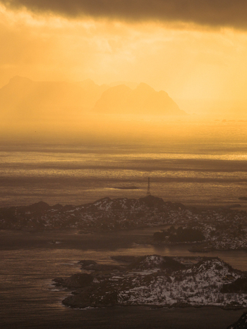 Aerial view of a landscape where the water meets the snow capped mountains under a golden sky Reinebringen Nordland Norway.
