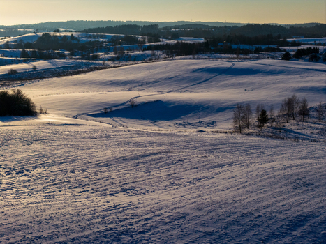 Aerial view of snow covered rolling hills and fields with long shadows and tracks during golden hour in Lithuania. Aerial view of snow covered rolling hills and fields with long shadows and tracks during golden hour in Lithuania.
