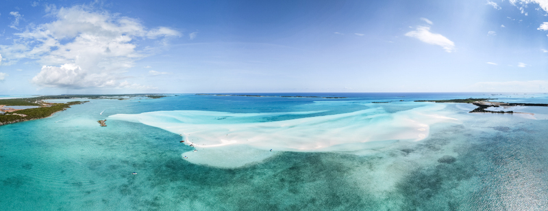 Aerial view of the Man O War Cay Sandbar stretching through turquoise waters near lush tropical islands under a blue sky in Rolletown Exuma The Bahamas. Aerial view of the Man O War Cay Sandbar stretching through turquoise waters near lush tropical islands under a blue sky in Rolletown Exuma The Bahamas.
