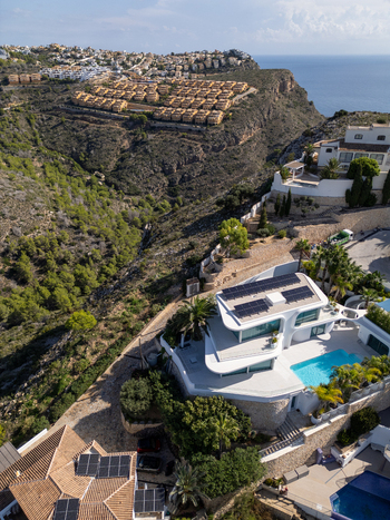 Aerial view of a modern luxury villa with a swimming pool and solar panels situated on a hillside overlooking the Mediterranean coast in Moraira Valencian Community Spain.