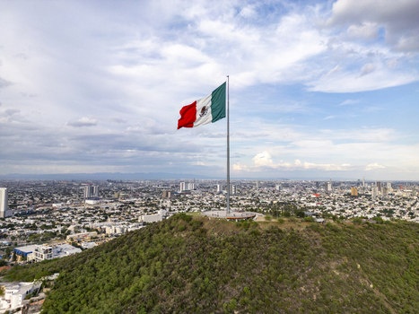Aerial view of the Mexican flag waving atop the Cerro del Obispado overlooking the urban landscape of Monterrey Nuevo Leon Mexico.