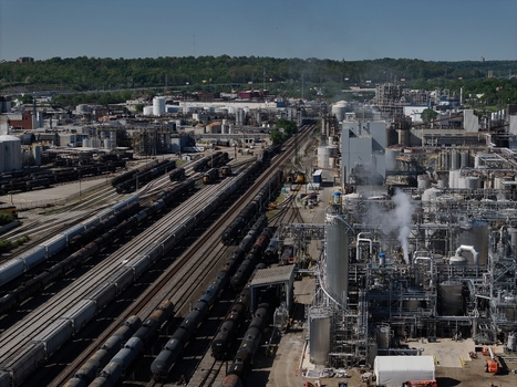 Aerial view of an industrial chemical plant with freight trains on multiple tracks and steam rising from processing units Cincinnati OH United States. Aerial view of an industrial chemical plant with freight trains on multiple tracks and steam rising from processing units Cincinnati OH United States.