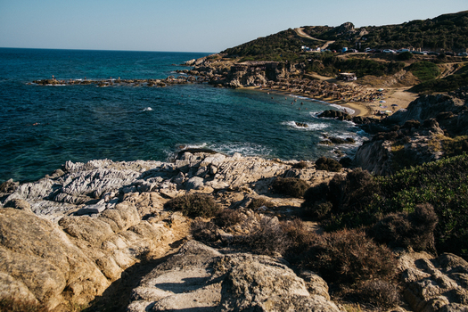 View of Tigania Beach with rocky cliffs sandy shoreline sun umbrellas and clear blue water in Chalkidiki Greece.