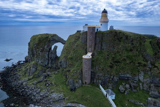 Aerial view of Sanda Island Lighthouse on a rocky cliff with a natural rock arch and green grass near the Mull of Kintyre Argyll and Bute Council Scotland United Kingdom.
