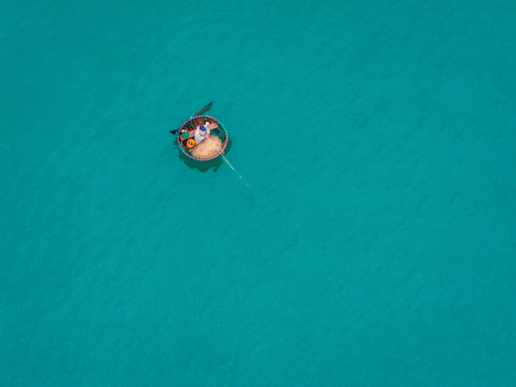 Aerial view of a traditional round basket boat with a fisherman floating on the clear turquoise water of the sea in Vietnam. Aerial view of a traditional round basket boat with a fisherman floating on the clear turquoise water of the sea in Vietnam.