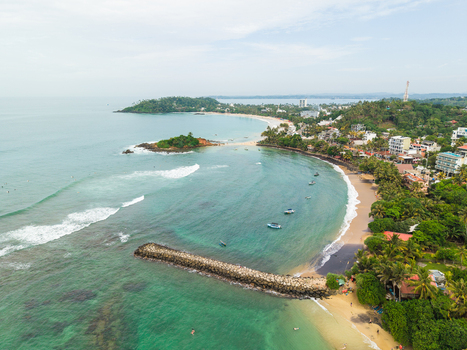 Aerial view of Parrot Rock surrounded by turquoise ocean waves a sandy beach and lush palm trees in Mirissa Southern Province Sri Lanka. Aerial view of Parrot Rock surrounded by turquoise ocean waves a sandy beach and lush palm trees in Mirissa Southern Province Sri Lanka.