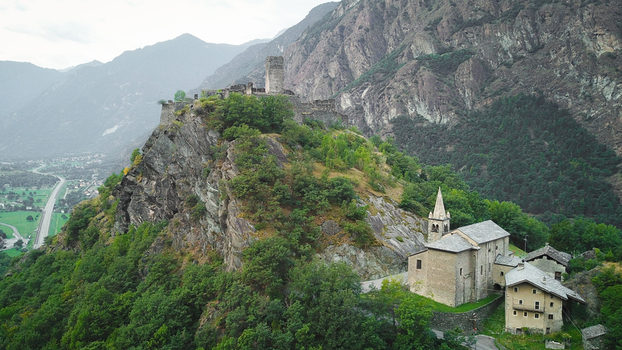 Aerial view of the historic Saint Germain Castle ruins and church perched on a rocky cliff surrounded by lush green mountains in Montjovet Aosta Valley Italy.